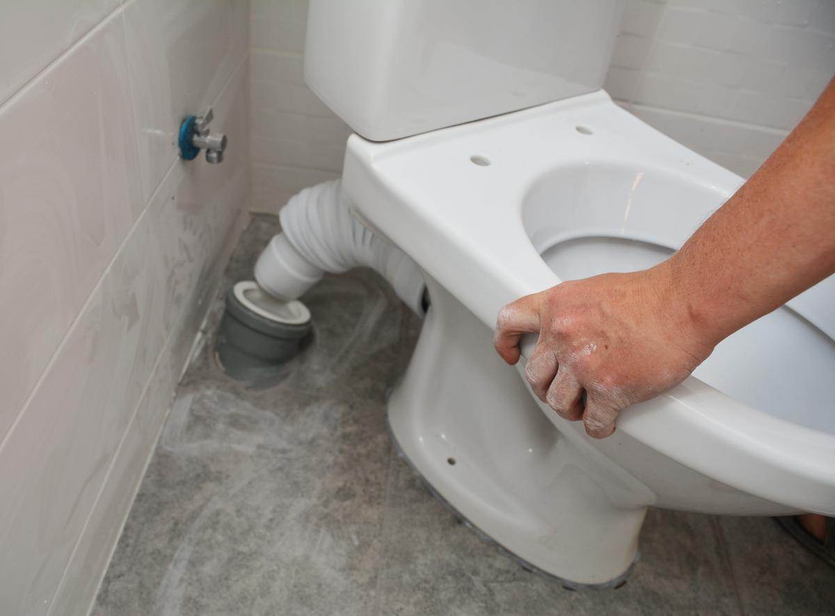 Victor, a professional plumber from Victor Plumbing, meticulously cleans a toilet in a bathroom.