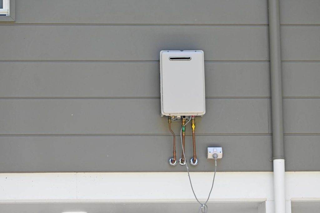 Victor Plumbing installs a water heater on the side of a building.